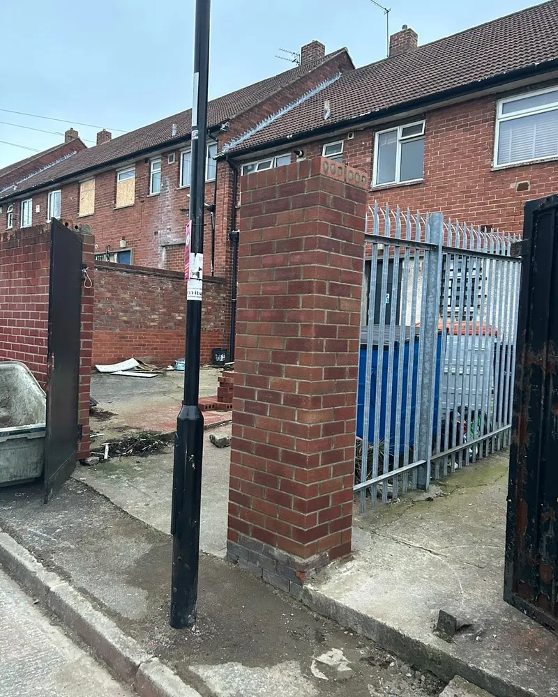 New brick pillar between two back-lane gates, finished with a brick-on-edge cap
